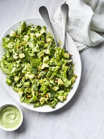Pavasarinės žalios salotos pateikiamos serviravimo lėkštėje ir patiekiamos su žaliu padažu.